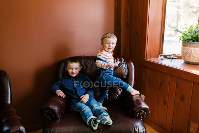 Two brothers playing together on arm chair in orange red living room — Stock Photo