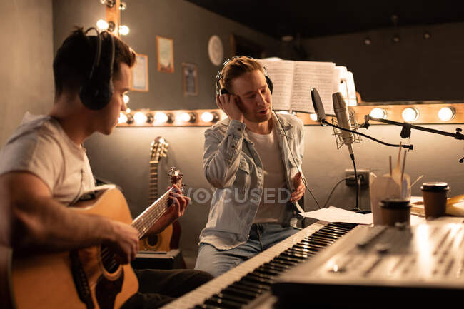 Чоловік співак і гітарист створюють пісню разом у сучасній творчій студії — стокове фото
