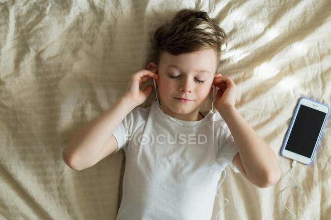 Мальчик слушает музыку с наушниками на кровати — стоковое фото