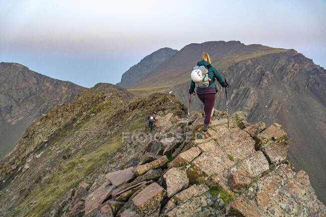 Vista trasera del excursionista femenino con bastones de senderismo en las rocas en la montaña - foto de stock
