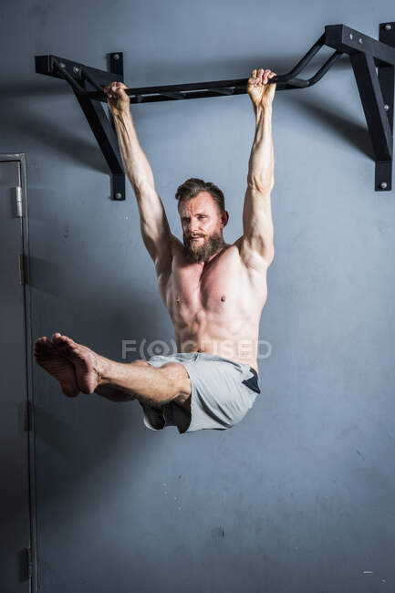 Homem com barba pendurado em barra de puxar para cima no ginásio — Fotografia de Stock