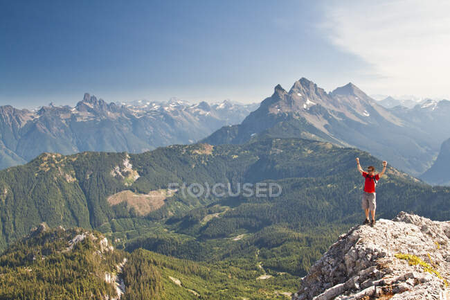 Hiker reaches summit of mountain, celebrates with arms raised. — Stock Photo