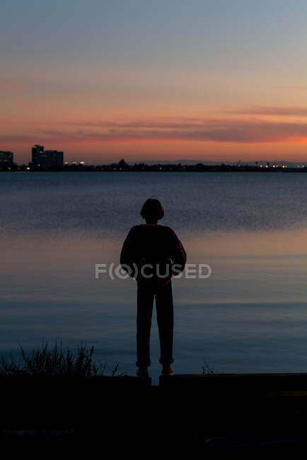 Silhouette eines jungen Menschen, der bei Sonnenuntergang über die Bucht auf die Stadt blickt — Stockfoto