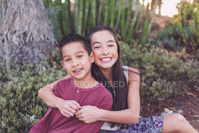 Older sister hugging young brother by a cactus garden — Stock Photo