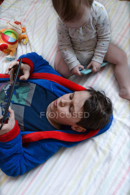 Baby girl sitting next to brother that playing on tablet — Stock Photo
