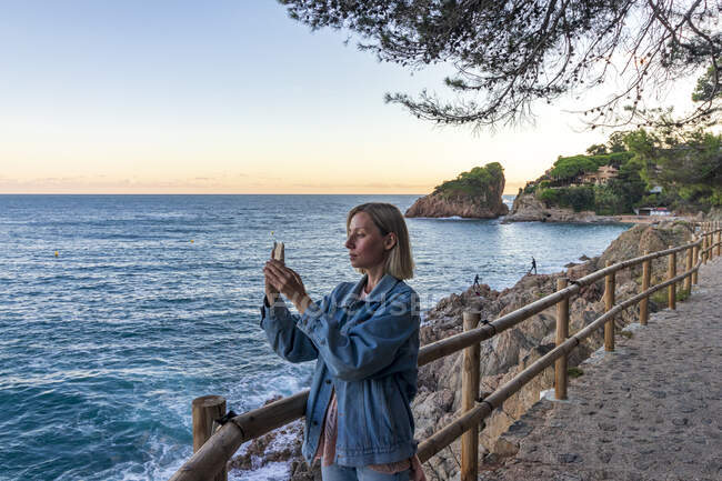Mujer joven tomando fotos en la playa - foto de stock