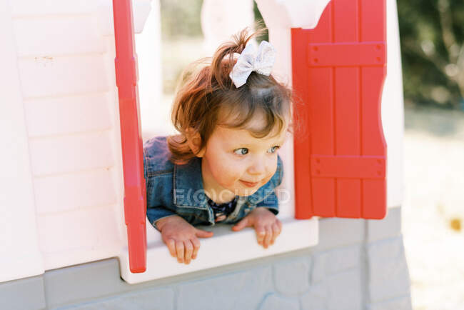 Petite fille tout-petit regardant par la fenêtre de sa maison de jeu dans la cour — Photo de stock