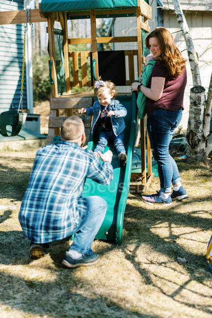 A young family playing in the backyard with a playground set together — Stock Photo