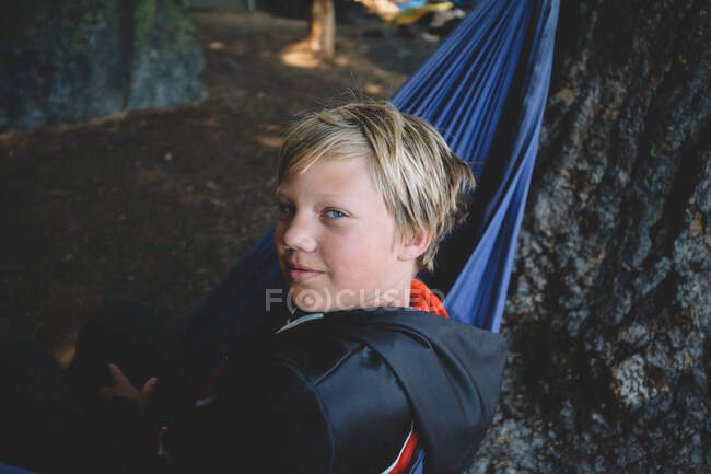 Мальчик-блондин смотрит через плечо из фиолетового гамака — стоковое фото