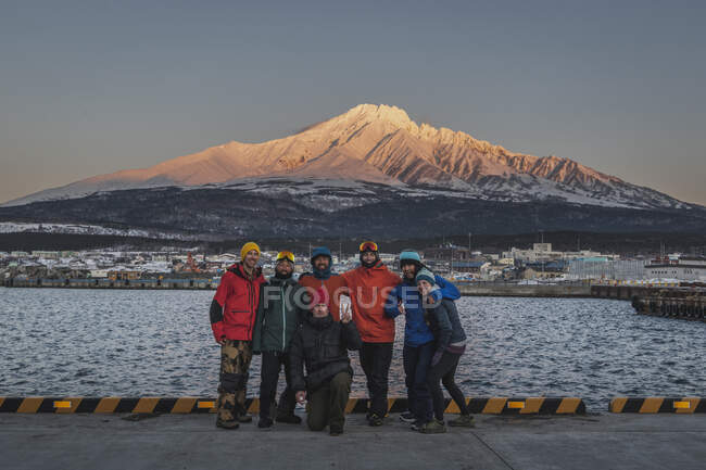 Porträt von lächelnden Männern und Frauen in warmer Kleidung, die am Hafen vor einem schneebedeckten Berg stehen — Stockfoto