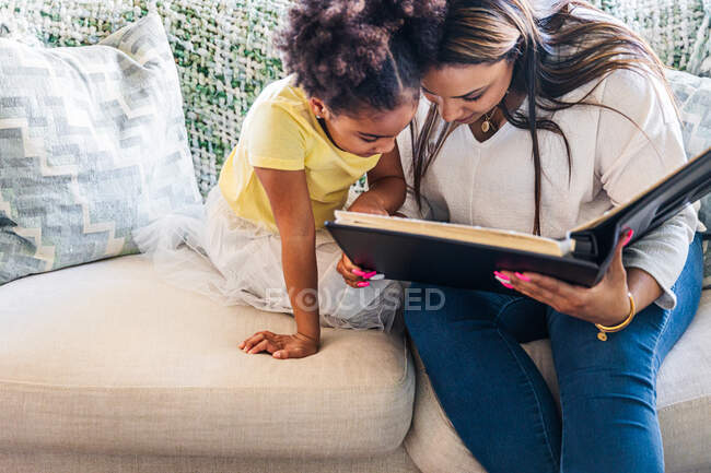 Мати дивиться на фотоальбом з дочкою, сидячи на дивані у вітальні — стокове фото