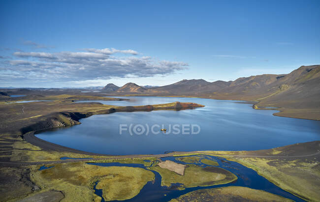 Drone view of calm lake with clean water located in wetland near mountain range against cloudy blue sky — Stock Photo