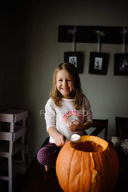 Girl carving pumpkin and scooping out seeds on her kitchen table home — Stock Photo