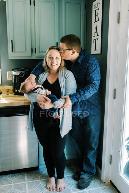 A young mother and father with their newborn baby son in kitchen — Stock Photo