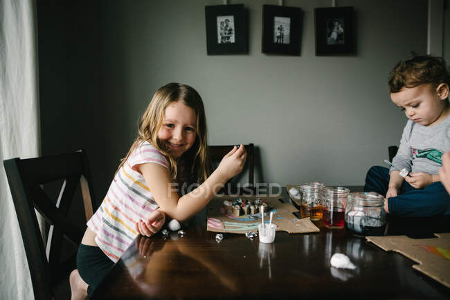 Девушка улыбается во время художественного проекта за столом со своими братьями и сестрами — стоковое фото