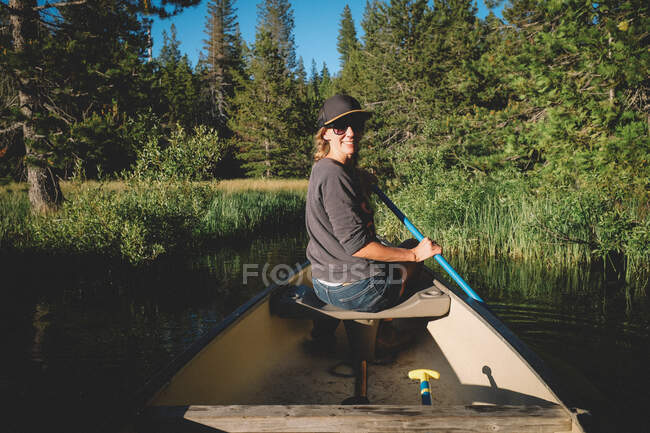 Mulher olha por cima do ombro enquanto rema em uma canoa — Fotografia de Stock