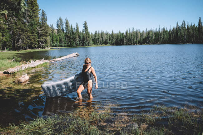 Mulher loira emerge do lago em terno preto segurando uma flutuação — Fotografia de Stock