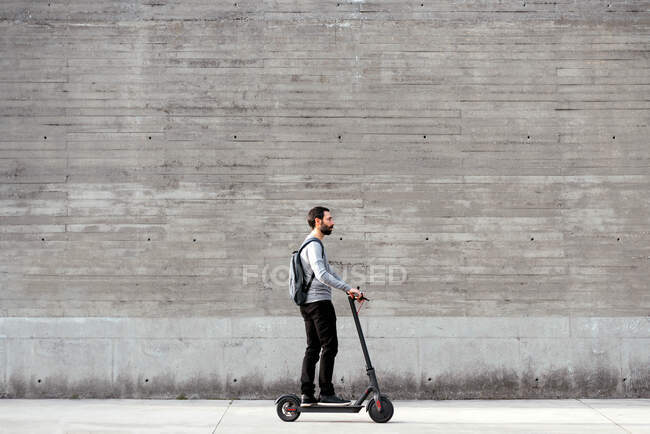 Hombre montando scooter eléctrico en frente de la pared gris - foto de stock