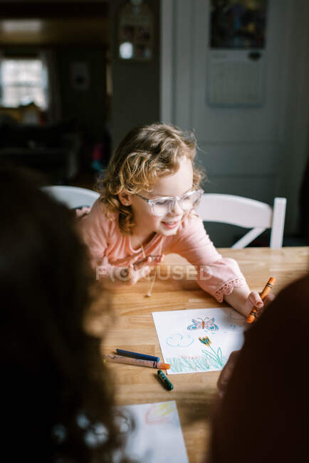 Дитяча дівчинка в окулярах розмальовка зі своєю сім'єю за столом — стокове фото