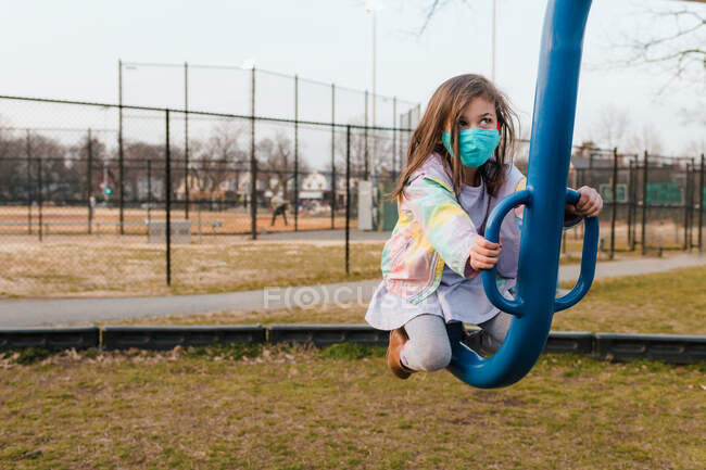 Kleines Mädchen mit Mundschutz spielt auf Säge auf Spielplatz — Stockfoto
