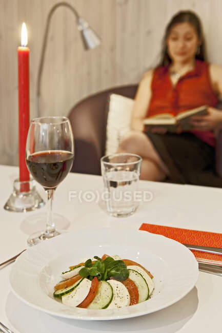 Ensalada caprese en la mesa con la mujer leyendo en el fondo - foto de stock