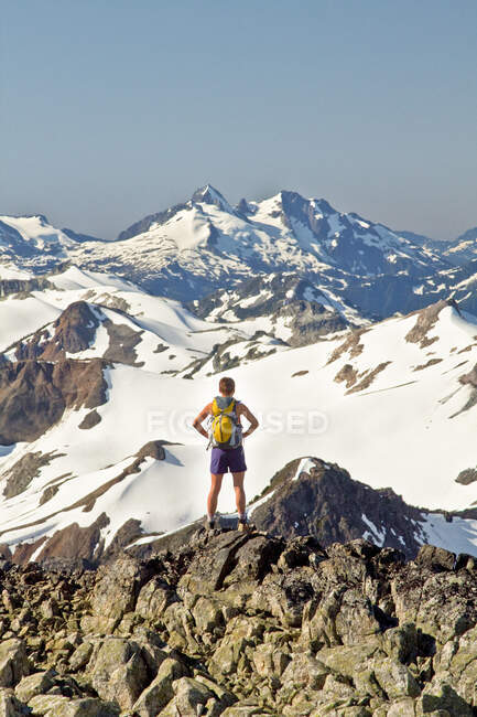 Rear view of attractive fit woman on mountain summit wearing backpack. — Stock Photo