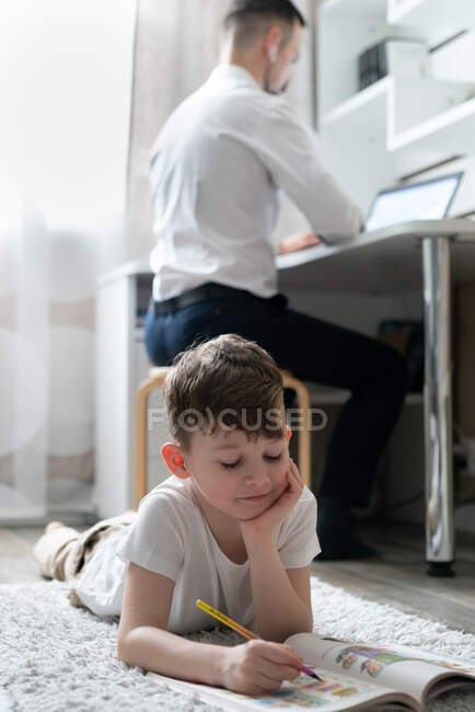 Junge macht Hausaufgaben in der Nähe des arbeitenden Vaters — Stockfoto