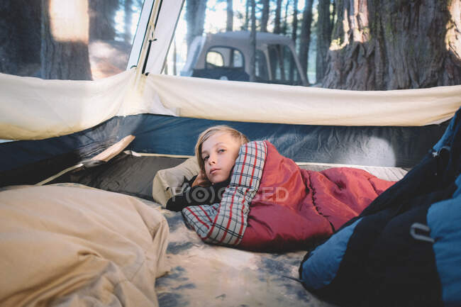 Sleepy Boy avvolto nel sacco a pelo si sveglia nel bosco — Foto stock