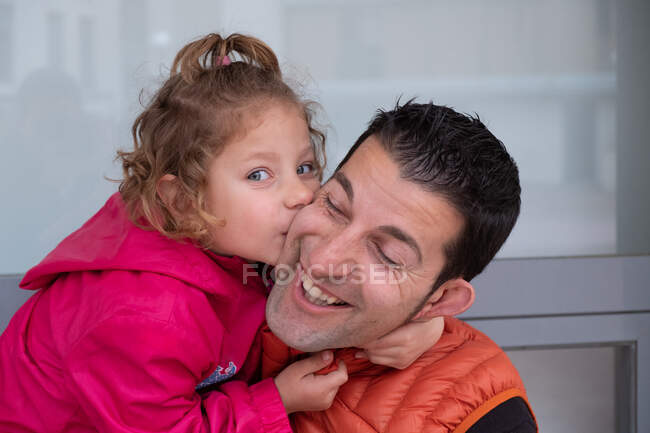 Una niña de 4 años abrazando a su padre de la mano y besándose - foto de stock