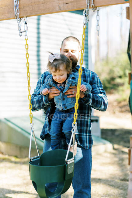 Um pai colocando sua filha criança em um balanço de bebê em seu quintal — Fotografia de Stock