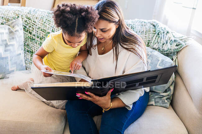 Мати і дочка дивляться фотоальбом, сидячи на дивані вдома — стокове фото