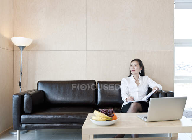 Mujer de negocios sentada en sofá de cuero dentro de chalet en Islandia - foto de stock