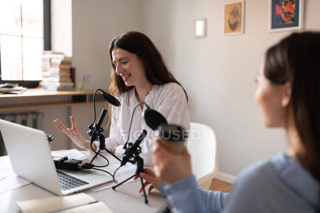 Happy woman smiling and speaking into microphone during podcast with friend — Stock Photo