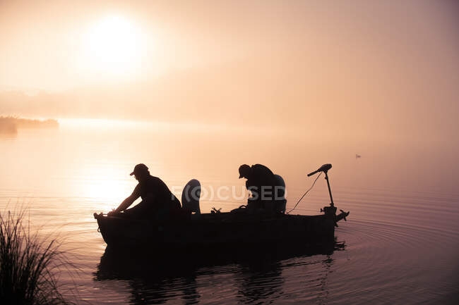 Silhouette Bootsfahrer auf idyllischem See bei buntem nebligem Sonnenaufgang — Stockfoto