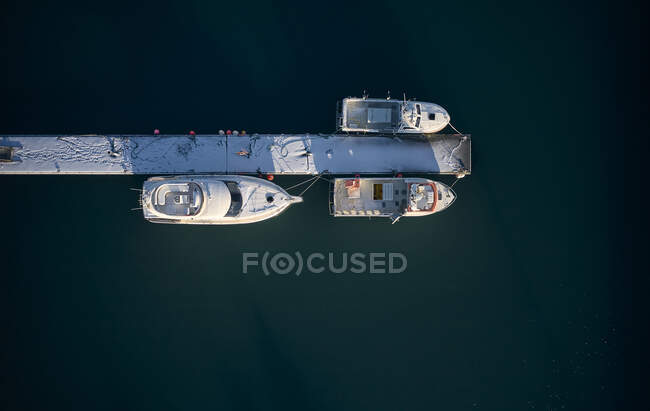 Drone vista dall'alto di poche barche a vela a stretto molo coperto di neve in acqua fredda di mare — Foto stock
