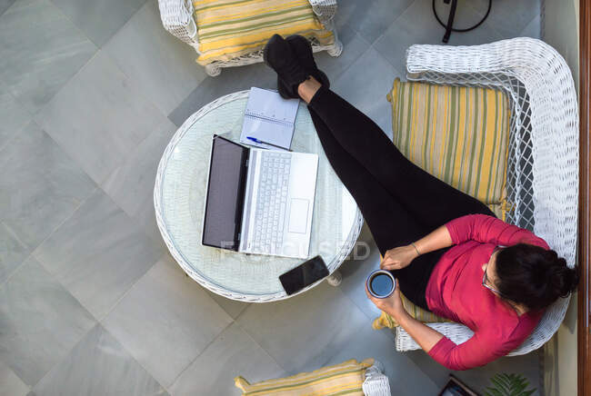 Draufsicht einer Frau, die sich bei einer Tasse Kaffee entspannt, während sie einen Computer zu Hause benutzt. — Stockfoto