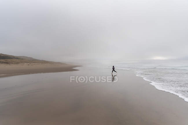 One person striding away from edge of ocean waves on overcast day — Stock Photo
