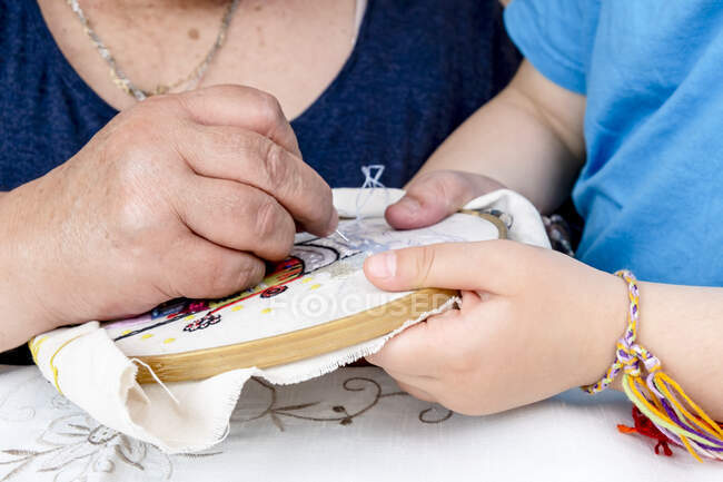 Крупный план рук девушки и ее бабушки, делающих вышивку — стоковое фото