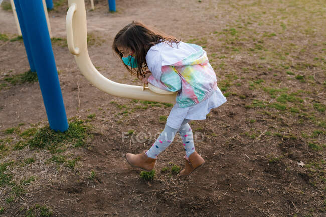 Mädchen mit Gesichtsmaske spielt in Kleid und Stiefeln auf Spielplatz — Stockfoto