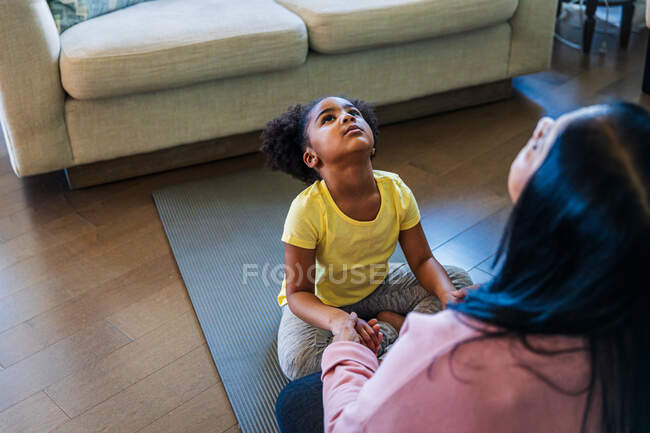Girl practicing yoga with grandmother while sitting on exercise mat in living room — Stock Photo