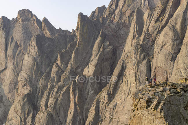 Mochileros masculinos y femeninos de pie sobre rocas contra el acantilado mientras caminan en vacaciones - foto de stock