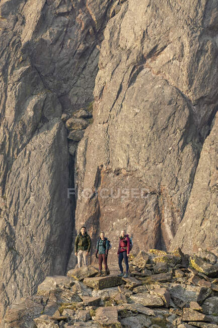 Amis masculins et féminins debout sur des rochers contre une falaise en randonnée en vacances — Photo de stock