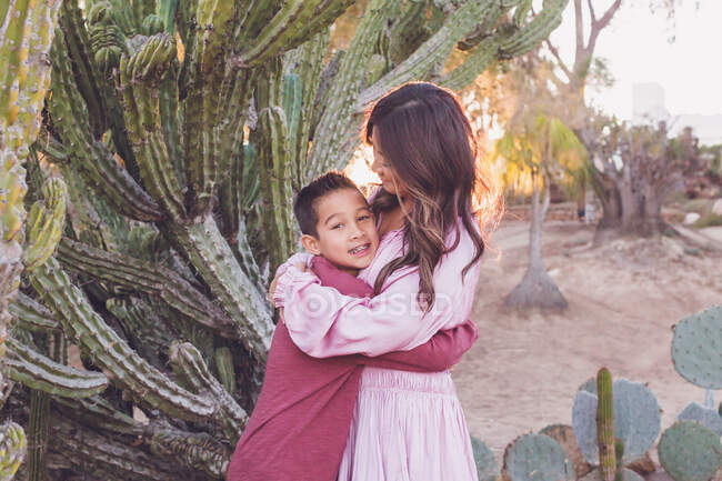 Madre che abbraccia il figlio davanti a un grande cactus con sole retroilluminato. — Foto stock