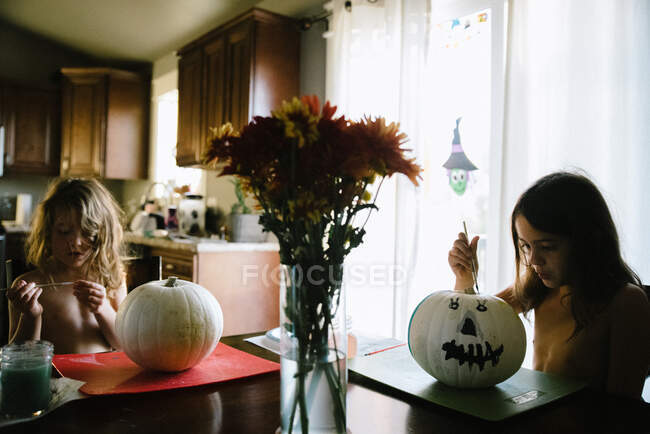 Dos hermanas pintando calabazas para Halloween en la mesa de la cocina - foto de stock
