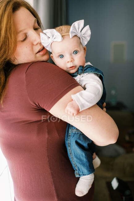 A little baby girl in her mother's arms looking on with surprise — Stock Photo