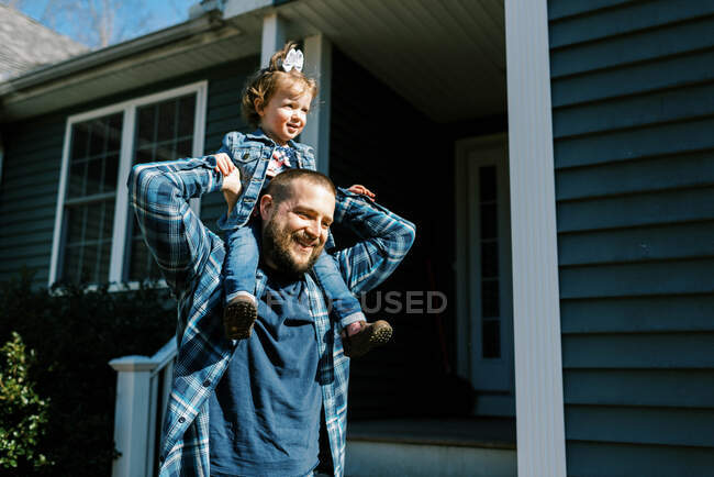 Young father carrying his toddler daughter on shoulder around house — Stock Photo