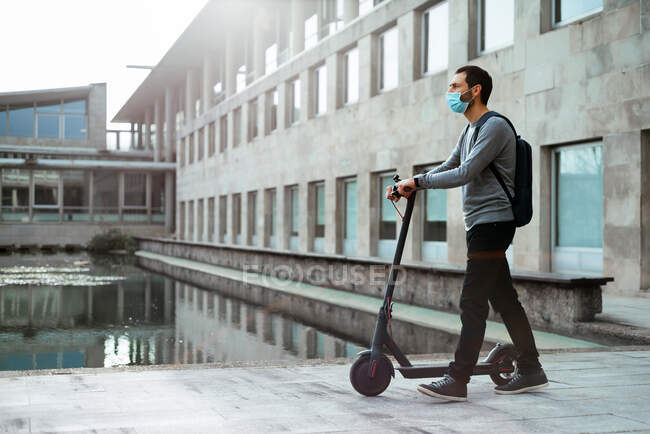 Elegante hombre caminando cerca de scooter eléctrico en la ciudad moderna - foto de stock