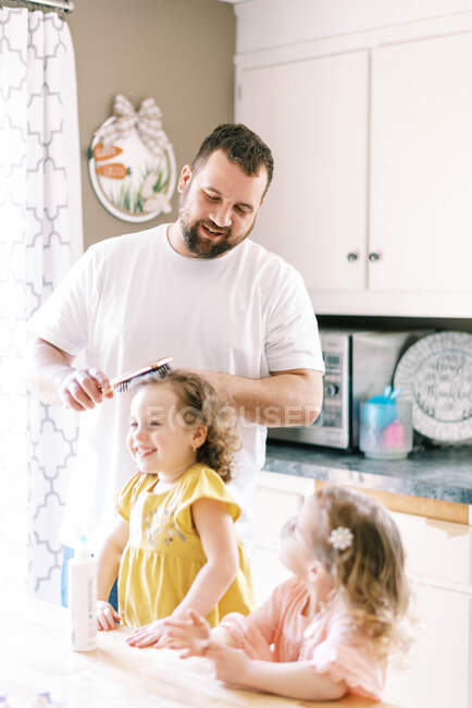 A father caring for his twin daughters by styling hair for school — Stock Photo