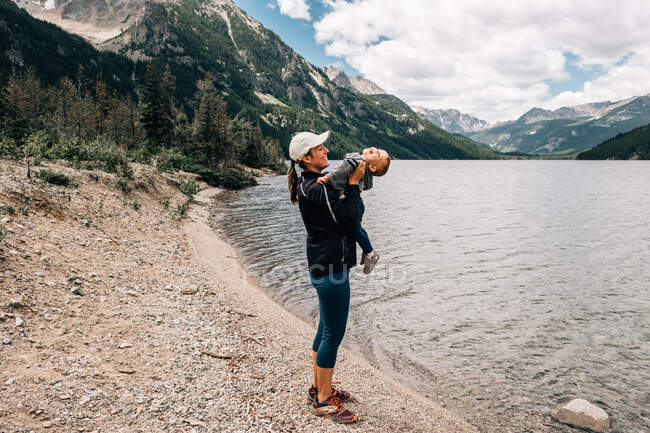 Mamma gioca con il figlio del bambino in una catena montuosa vicino a un lago — Foto stock
