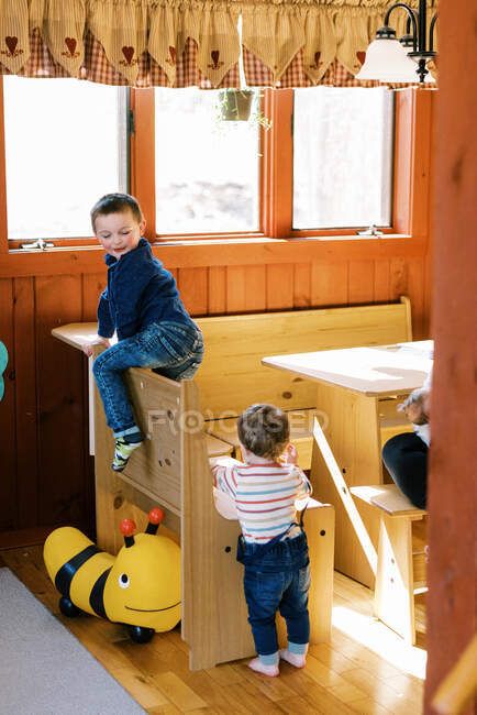 Dos niños pequeños escalando en su comedor en una mañana soleada - foto de stock